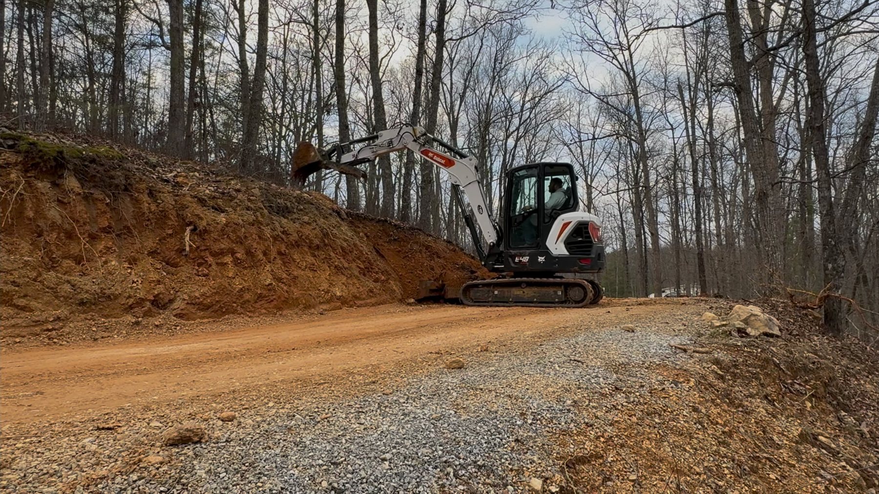 Excavator working near a gravel drive during site preparation