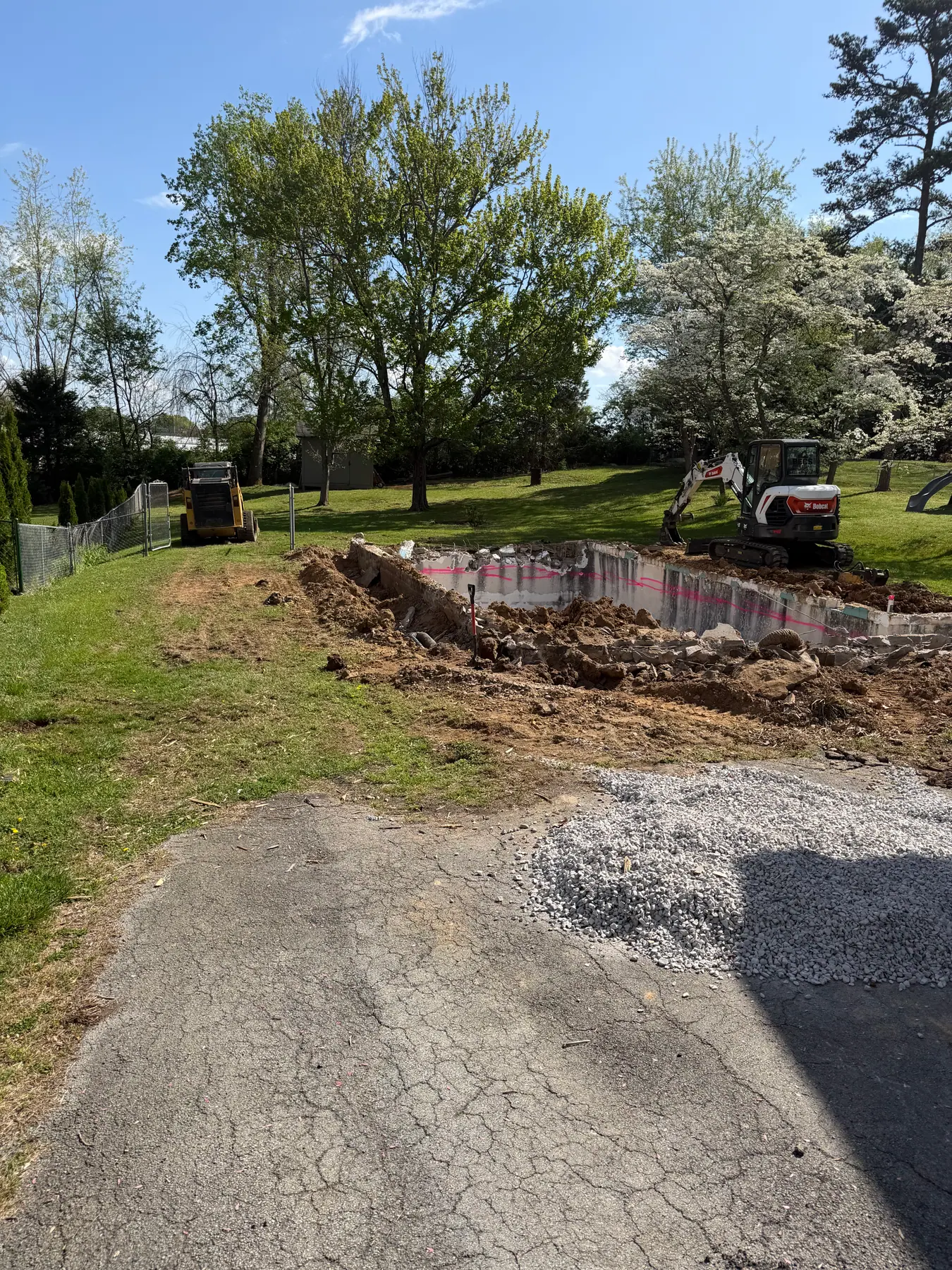 Excavator removing an in-ground pool shell and surrounding concrete