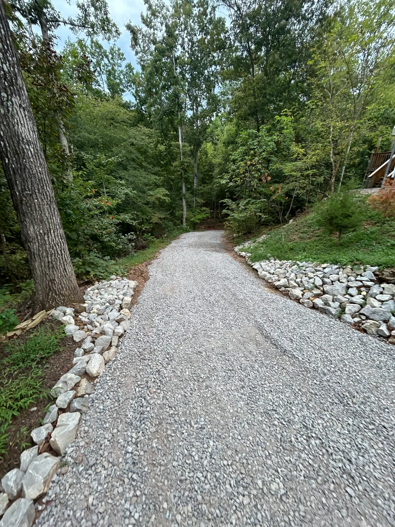 Fresh gravel driveway curving between trees with stone edging