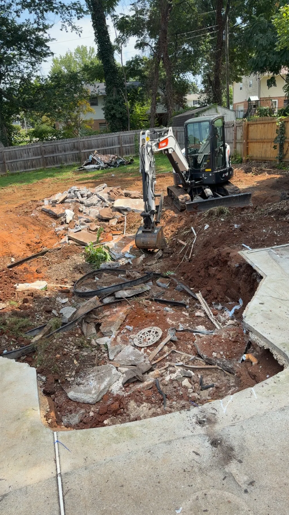 Excavator breaking up a pool and surrounding concrete beside a deck